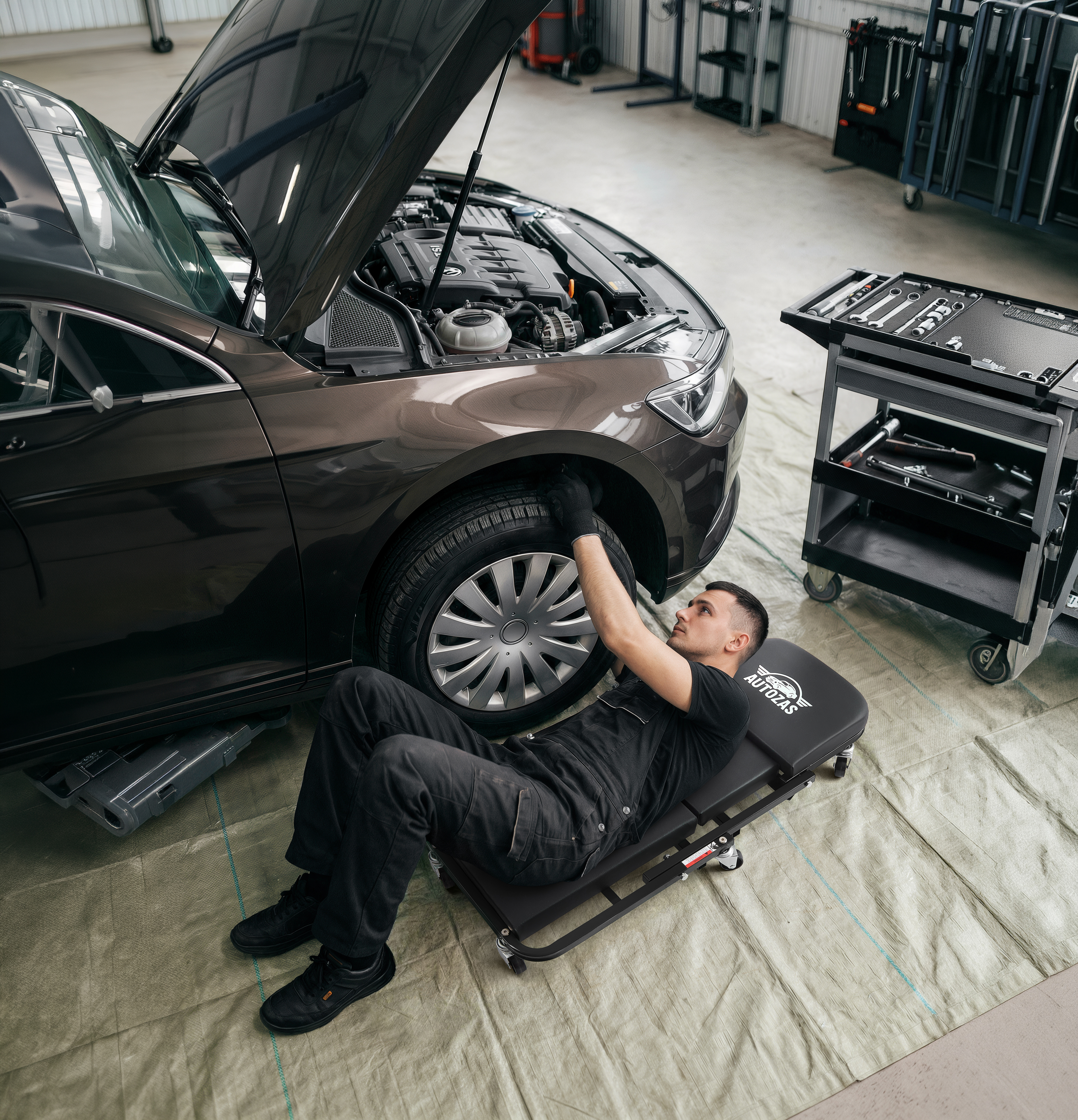 Autozas-branded mechanic lying on the Black 2-in-1 creeper in convertible mode — demonstrating instant stool-to-creeper transformation