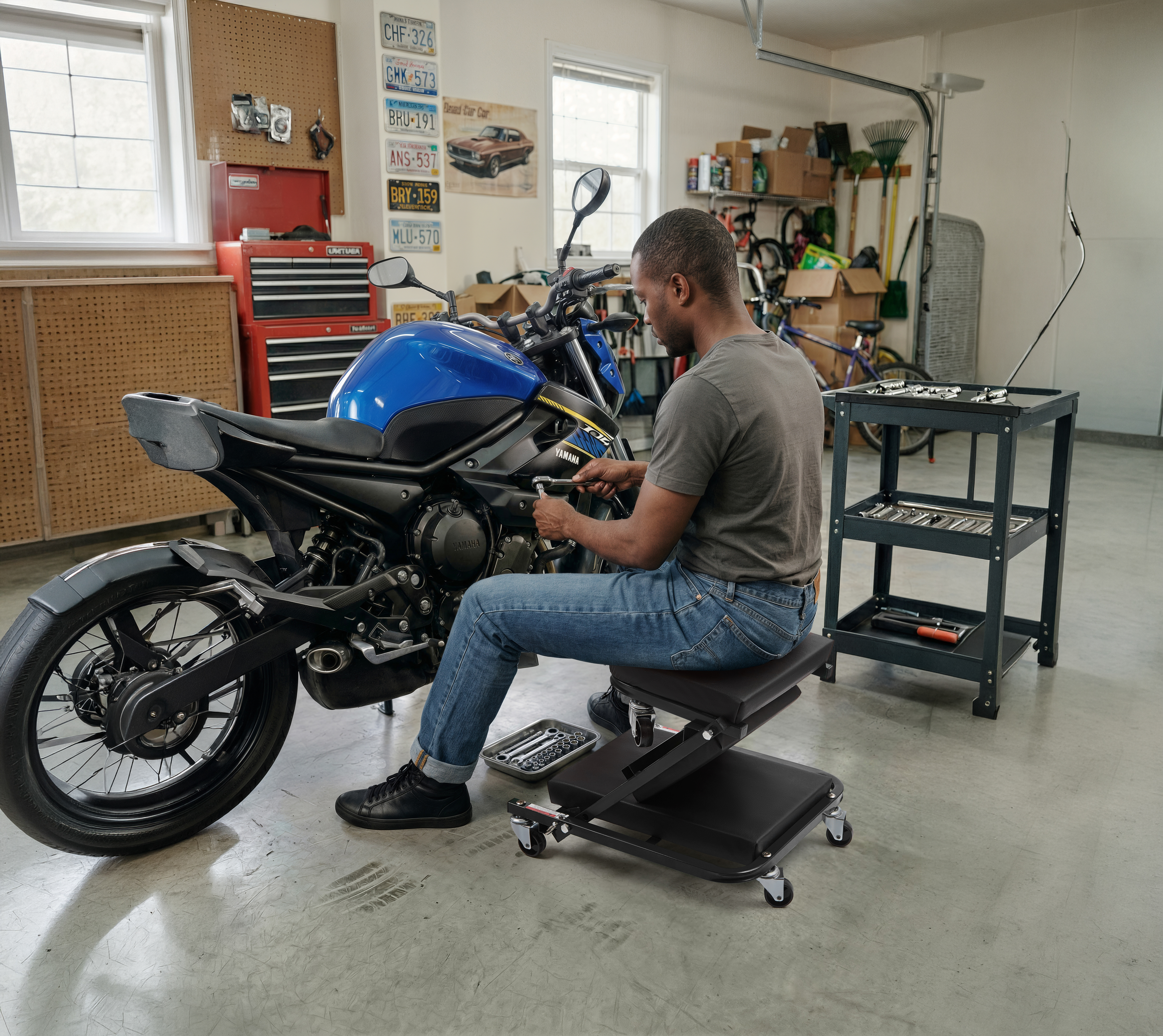 Mechanic seated on the Autozas Black shop stool servicing a Yamaha motorcycle — 360-degree swivel casters allow smooth movement on concrete